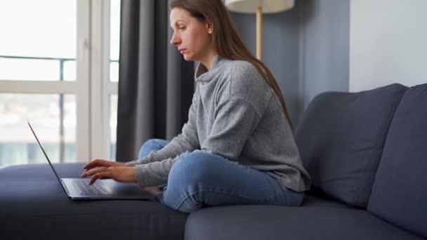 Woman sitting on a cozy sofa and working on a laptop. Concept of remote work. - Filmmaterial, Video