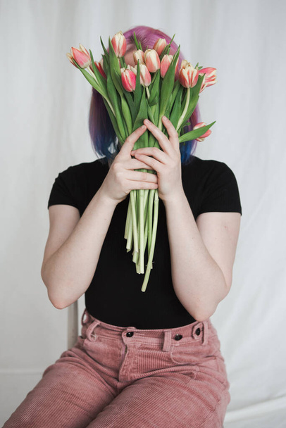 Girl with pink hair covers her face with a bouquet of tulips - 写真・画像