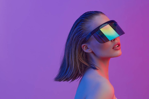 Cool stylish girl with a fashionable hairstyle and stylish glasses with a large glass poses on a bright neon background. - Foto, imagen