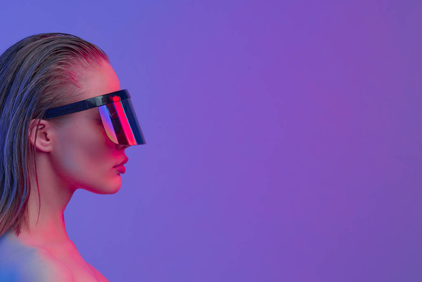 Cool stylish girl with a fashionable hairstyle and stylish glasses with a large glass poses on a bright neon background. - Foto, Bild