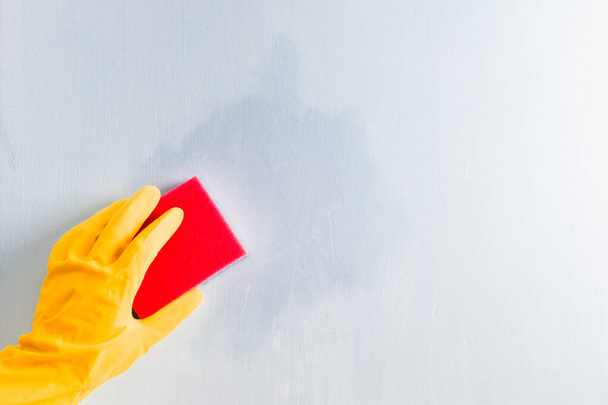 hand in a rubber yellow glove wipes a stain on the wall with a sponge, light blue background, copy spac - Photo, Image