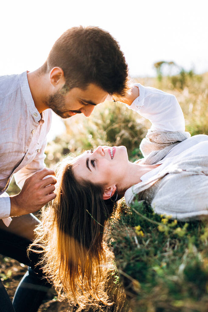 Retrato de una hermosa pareja tendida en la hierba. Tocar suavemente en la cara, abrazar y besar a la chica. Agárrate las manos - Foto, imagen