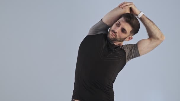 A slim young athletic man in sportswear doing warming-up exercise isolated over gray background in studio - Filmati, video