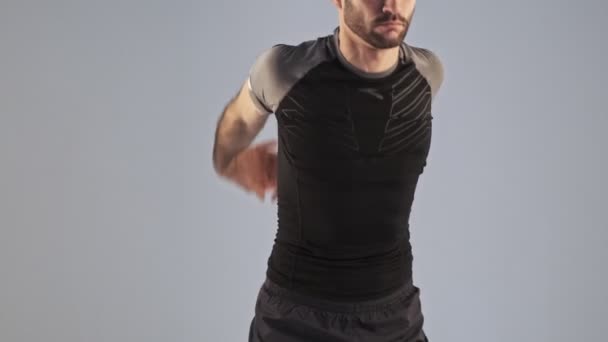A serious young athletic man in sportswear is doing slopes exercise isolated over gray background in studio - Filmati, video