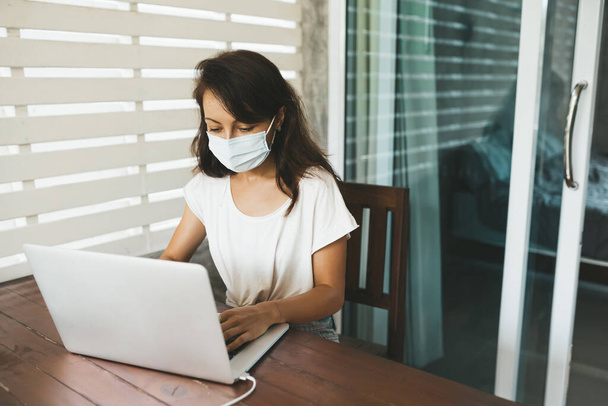 Woman in medical mask sitting at the desk and typing in laptop. Copy space - Foto, imagen