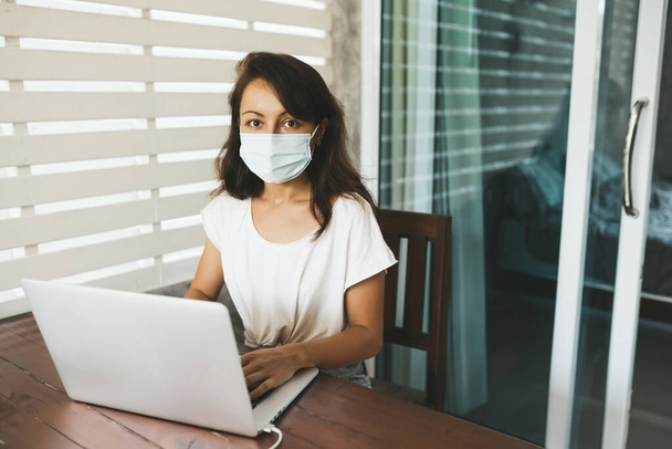 Woman in medical mask sitting at the desk and typing in laptop. Copy space - Fotoğraf, Görsel