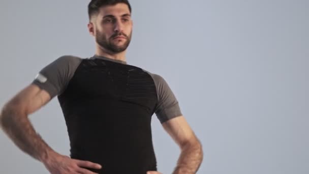A calm young athletic man in sportswear is doing circle exercises isolated over the grey background in studio - Filmati, video