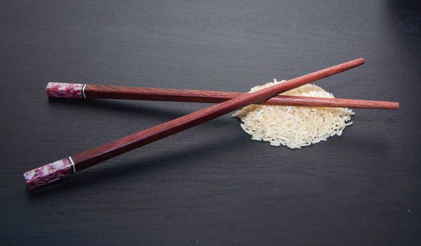 Baguettes en bois croisées sur du riz basmati sur fond sombre
. - Photo, image