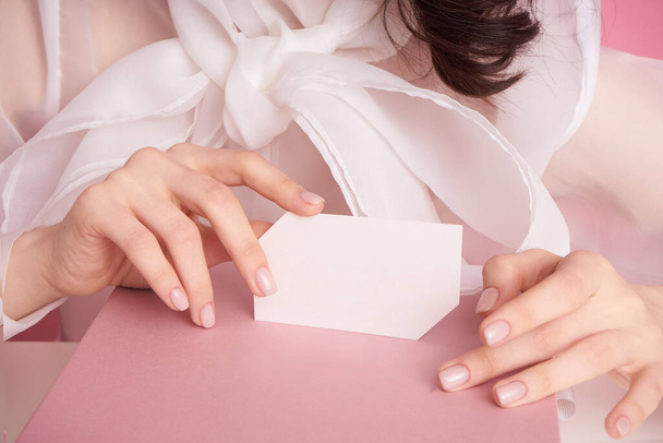  close-up female hand on a pink background holds an empty sheet to fill - Φωτογραφία, εικόνα