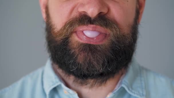 Close-up van een man met een baard die kauwgom kauwt. Een man blaast een bel kauwgom uit. - Video