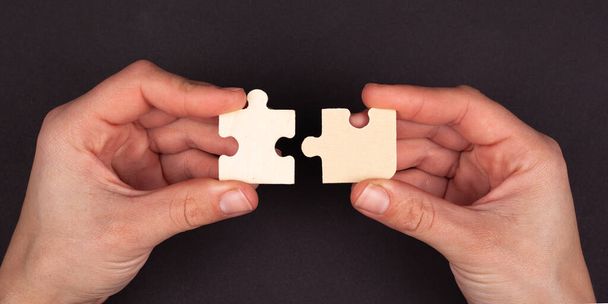 handen bundelen puzzelmozaïek op een zwarte achtergrond. symbool van associatie en communicatie. bedrijfsstrategie concept close-up  - Foto, afbeelding