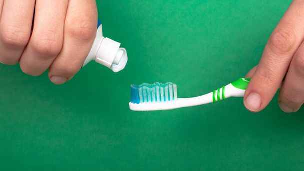hand knijpt een tandpasta op een tandenborstel op een groene achtergrond close-up. tandheelkundige en mondverzorging tandbederf - Foto, afbeelding