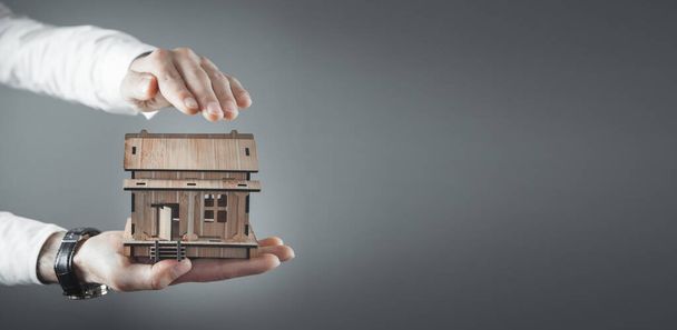 Male hands protect wooden house model. - Photo, Image