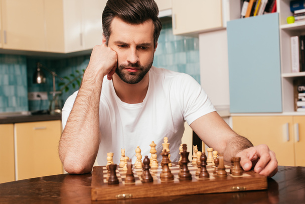 Foco seletivo de homem pensativo sentado perto do xadrez no tabuleiro de xadrez na mesa
  - Foto, Imagem
