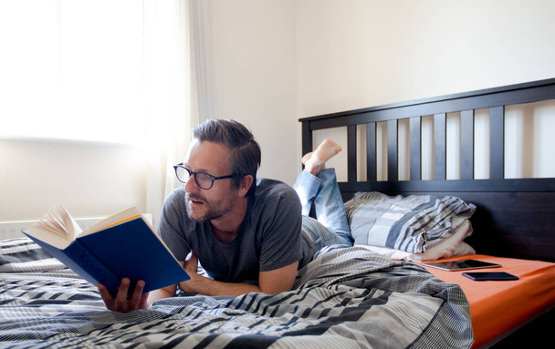 Человек, лежащий на кровати и читающий книгу
  - Фото, изображение