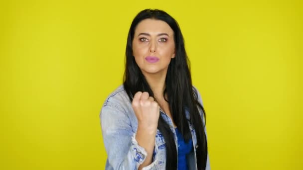 Mujer muestra un puño en la cámara sobre un fondo amarillo con espacio para copiar
 - Metraje, vídeo