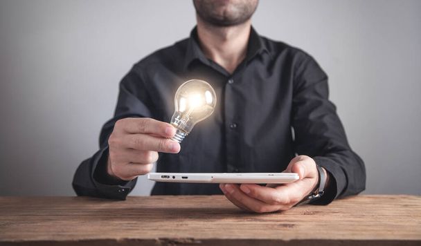 Muž držící žárovku s tabletou. Inspirace, technologie, tvořivost, podnikání - Fotografie, Obrázek