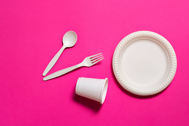 Sada biologicky rozložitelné jednorázové nádobí na růžovém pozadí. Lžíce, vidlička, talíř, sklenice kukuřičného škrobu. Ekologické. moderní ekologické biomateriály nahrazující plasty. - Fotografie, Obrázek