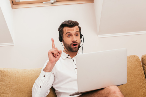 Evde bilgisayardaki görüntülü sohbet sırasında fikri olan heyecanlı kulaklıklı serbest çalışanın seçici odağı. - Fotoğraf, Görsel