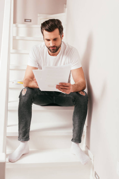 Handsome freelancer working with papers on stairs at home  - Foto, Imagem