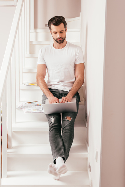 Handsome teleworker using laptop near papers on stairs  - Photo, Image