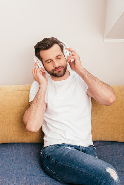 Handsome man listening music in headphones on couch at home  - Foto, Imagen