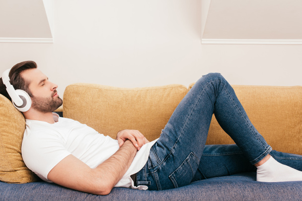 Vue latérale d'un bel homme écoutant de la musique dans un casque alors qu'il était allongé sur un canapé
  - Photo, image