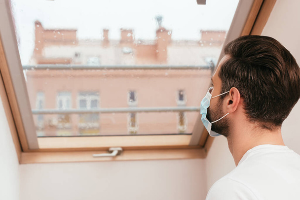 Back view of man in medical mask looking at window at home  - Valokuva, kuva