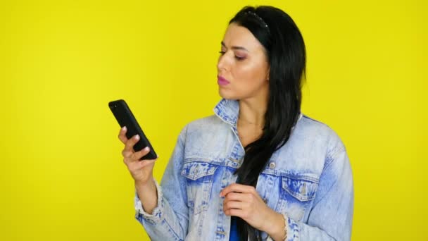 Woman uses a smartphone then is surprised and says wow on a yellow background - Záběry, video