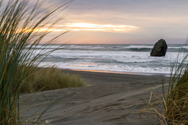Prachtige scène als de zon ondergaat aan de horizon en kleur toevoegt aan de donkere wolken en een beetje licht aan het zand en grassen gevonden in de kust van Oregon. - Foto, afbeelding