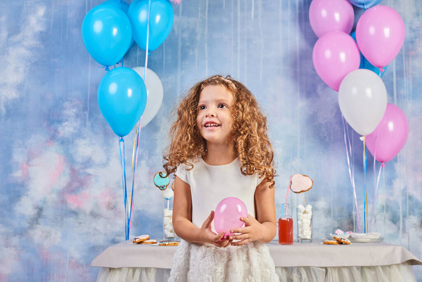 Children's funny birthday party in decorated room. Happy little girl celebrate International Children's Day. Funny child play at home - Photo, Image
