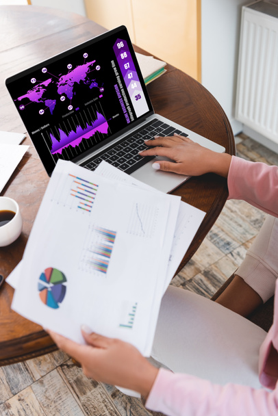 cropped view of african american freelancer holding documents near laptop with graphs  - Фото, изображение