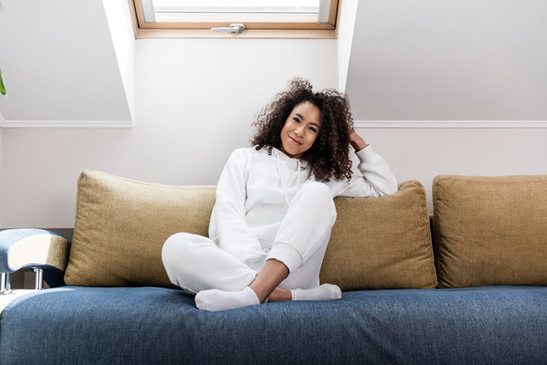 young african american woman smiling while sitting on sofa  - Фото, изображение