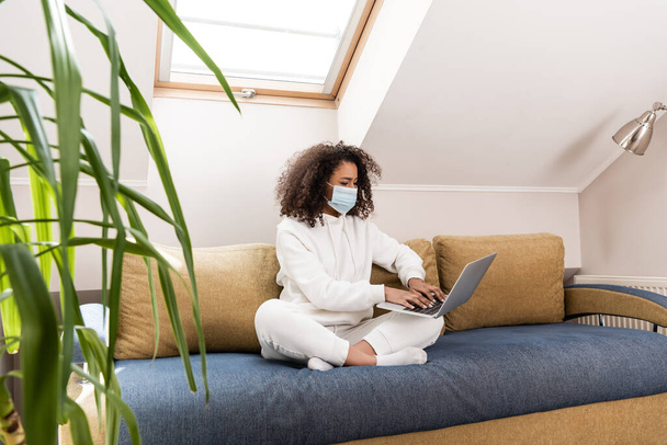 selective focus of young african american freelancer in medical mask using laptop  - Φωτογραφία, εικόνα