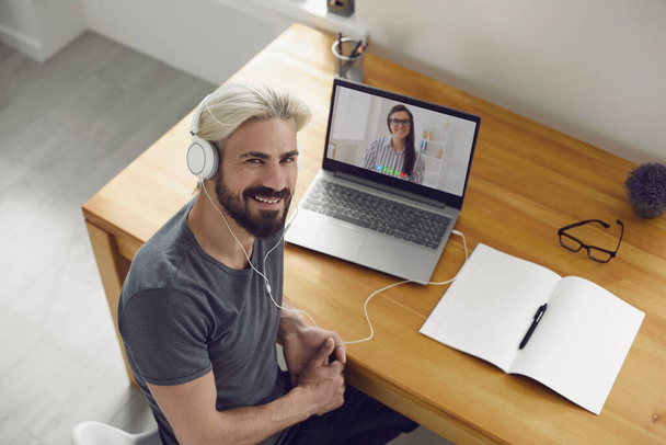 Education learning study online video call chat. Male student smiling is studying an online lesson with a teacher using a laptop webcam at home. - Foto, imagen