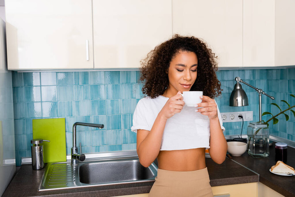 curly african american girl looking at cup of coffee  - Foto, afbeelding