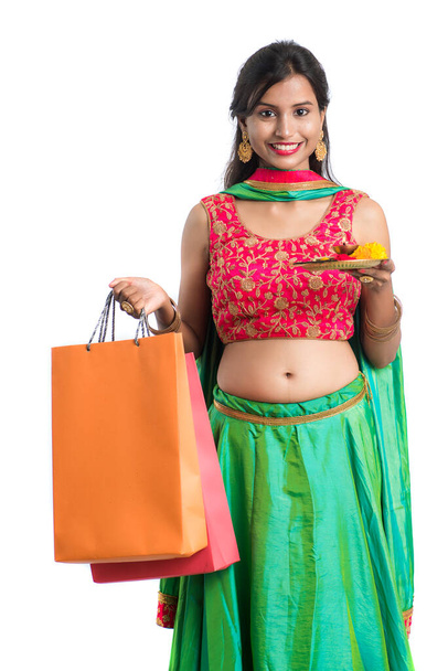 Beautiful Indian young girl holding and posing with shopping bags and pooja thali on a white background - Fotó, kép