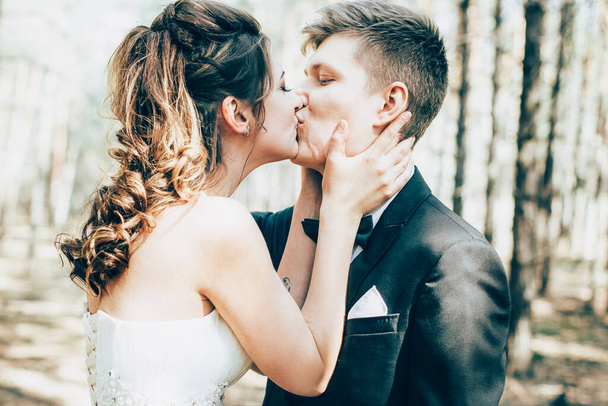 結婚式のカップル白いウェディングドレスの花嫁と新郎が森の中でキスをしキスをする - 写真・画像