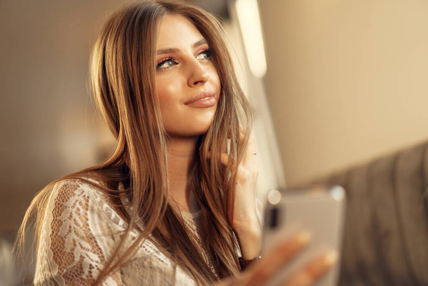 Szczęśliwa młoda kobieta za pomocą smartfona podczas siedzenia w stołówce - Zdjęcie, obraz