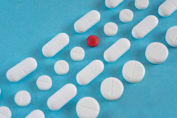 ένα κόκκινο χάπι με πολλά λευκά και κίτρινα χάπια σε μπλε φόντο. αντίγραφο χώρου - Φωτογραφία, εικόνα