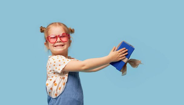 Advertising baby products. Portrait of surprised excited child girl with gift box. isolated over blue background. Empty space for text - Foto, immagini