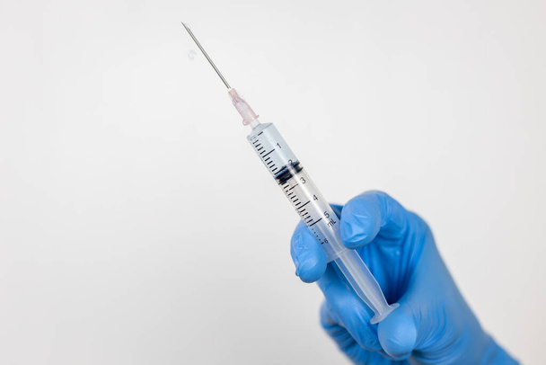 Healthcare concept with a hand in blue medical gloves holding Coronavirus vaccine in syringe. - Foto, Imagen