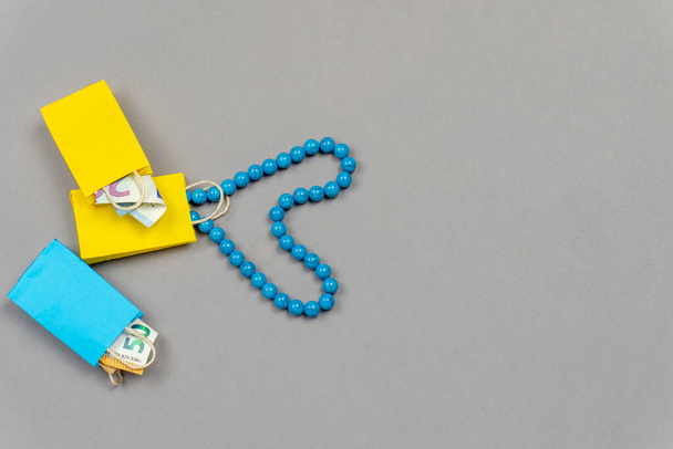 желтые и синие сумки с деньгами и синим ожерельем на сером фоне
 - Фото, изображение