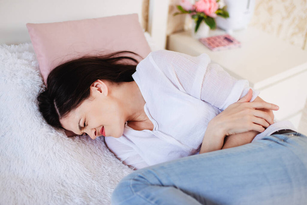 Woman at home on the bed is suffering from abdominal pain. Menstruation - Фото, зображення