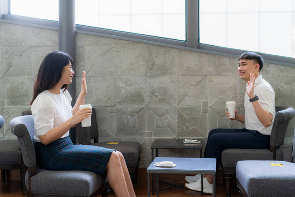 Azjatycki młody mężczyzna i kobieta siedzi jedna osoba na jednym stole i pozdrawiać i przywitać się na odległość 6 stóp odległość chronić przed COVID-19 wirusy dla społecznego dystansu dla ryzyka infekcji w kawiarni kawy - Zdjęcie, obraz