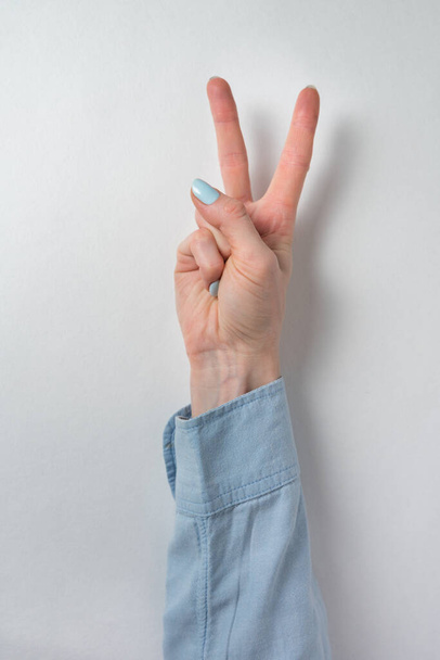 Mano femenina mostrando gesto de victoria. Dos dedos levantados sobre fondo blanco. Paz y victoria. Marco vertical
. - Foto, imagen