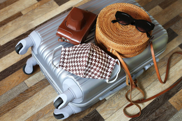 Suitcase hand bag with woman clothes and cotton face mask on wooden floor background. Preparing for trip abroad after corona virus pandemic. Travel concept. Prevention methods. - Foto, afbeelding