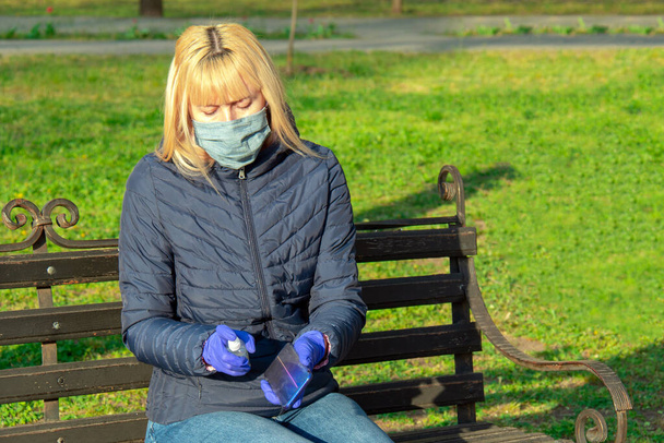 Mulher no parque Limpeza da tela do telefone móvel com a desinfecção toalhetes molhados Prevenção da contaminação por Coronavirus
. - Foto, Imagem