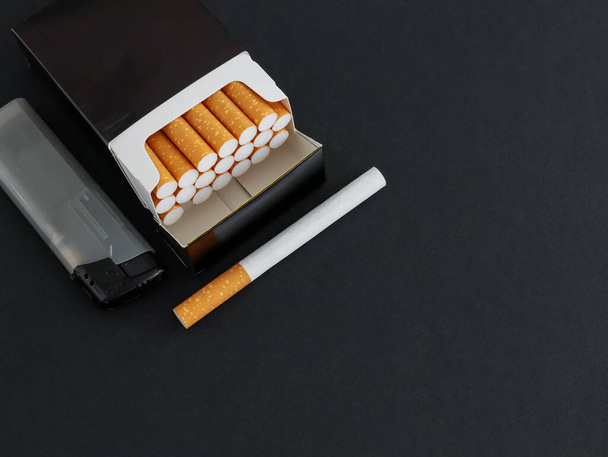 Zigarettenschachtel mit Feuerzeug auf schwarzem Hintergrund - Foto, Bild