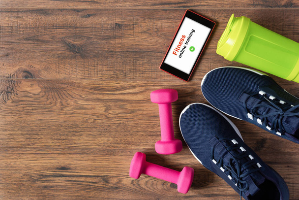 Fitness equipment, sport shoes and smartphone on wooden background top view. App for sport training indoors. Online Fitness training concept. Online workout staying at home. - Photo, Image